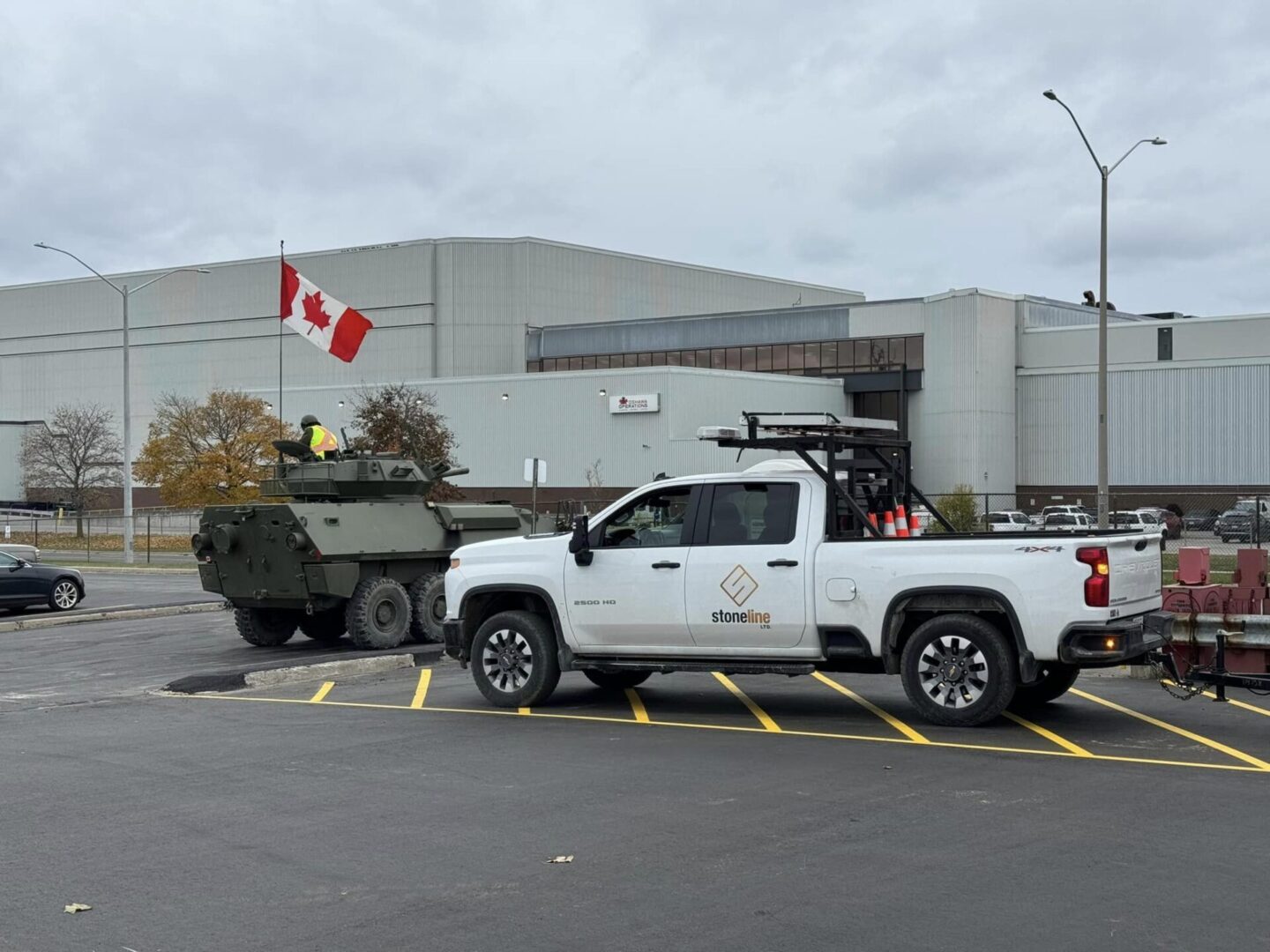 A army truck with a canadian flag passing through a parking lot